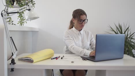 una mujer atractiva en su escritorio en la oficina escribe en su computadora portátil en un lugar de trabajo limpio y moderno