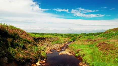 Low-aerial-shot-over-a-rock-natural-stream-in-the-countryside,-bright-blue-sky-day