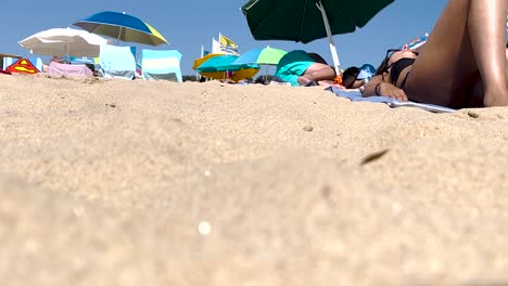 Una-Mujer-Descansa-En-La-Playa,-Mientras-El-Viento-Balancea-Suavemente-Las-Sombrillas-Detrás-De-Ella,-Creando-Un-Escenario-Tranquilo-De-Relajación-En-Medio-De-La-Brisa-Costera