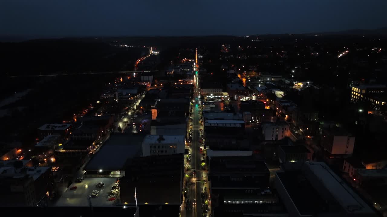 Ascending drone shot of illuminated main street of american town at night. Warm glowing lights of streetlamps on rainy autumn day. Wide shot. Quiet small town with straight roads,USA.