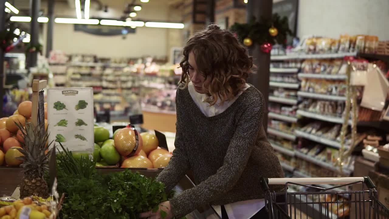 молодая женщина покупает органическую пищу в супермаркете. женщина берет зеленую свежую петрушку в продуктовом магазине. выбирает хороший бледный. медленный