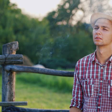 A-young-farmer-smokes-a-cigarette-stands-at-the-fence-of-the-ranch