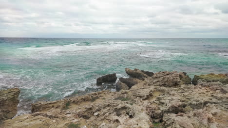 Rugged-coastline-with-jagged-rocks-and-turbulent-sea-waters-under-an-overcast-sky,-creating-a-dramatic-and-natural-seascape