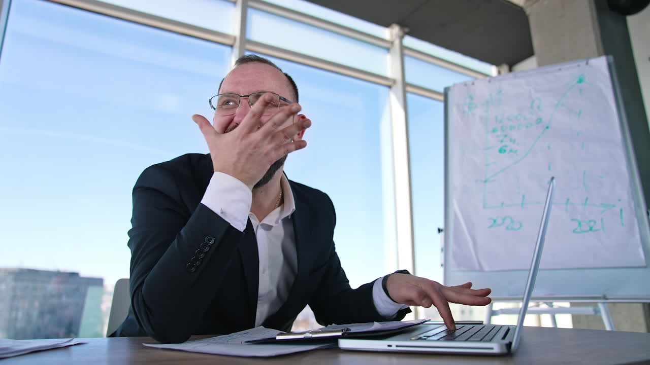 Funny businessman typing on a laptop. Office worker in glasses sitting at his desk in workplace and making mad face. Problems in business