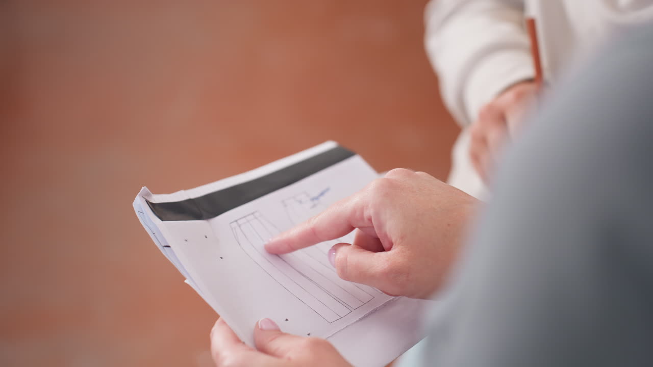 Closeup view of project manager pointing at trouser design sketch on white paper sheet while holding pencil during active teamwork planning creative clothing development session