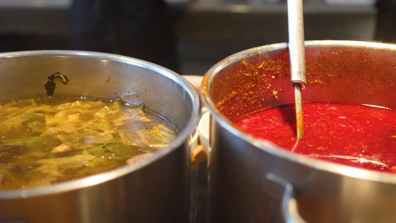 Un mestolo in acciaio inossidabile raccoglie uno stufato di curry rosso piccante del nord della Thailandia da una grande pentola.