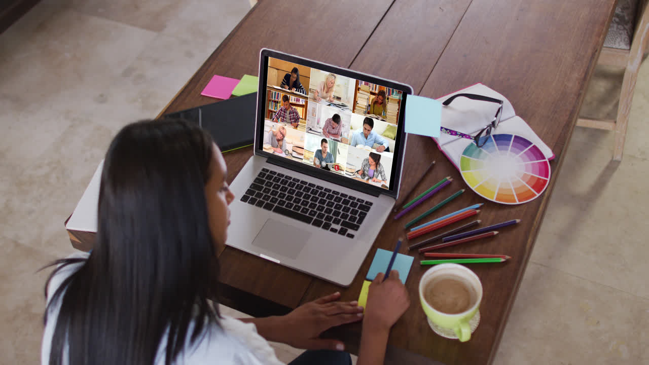 Maestra caucásica usando una laptop en videollamada con estudiantes, tomando notas