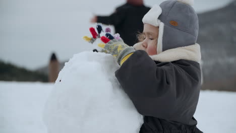 multi-ethnic baby girl playing an making big snowball during winter