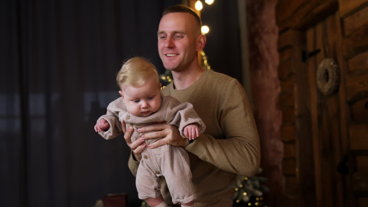 Happy man holding a cute blond baby. Dad blows on the child's hair. Smiling woman comes up to her beloved ones.