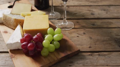 Video-of-cheeses-and-grapes-on-board-wine-bottle-and-glasses-on-wooden-table,-with-copy-space