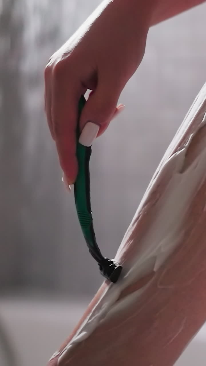 mujer se afeita el pelo de la piel de las piernas con una navaja de afeitar en el baño de primer plano. señora graciosa quita el pelo con la hoja en la unidad de ducha. mujer con espuma en la pierna y afeitador seguro