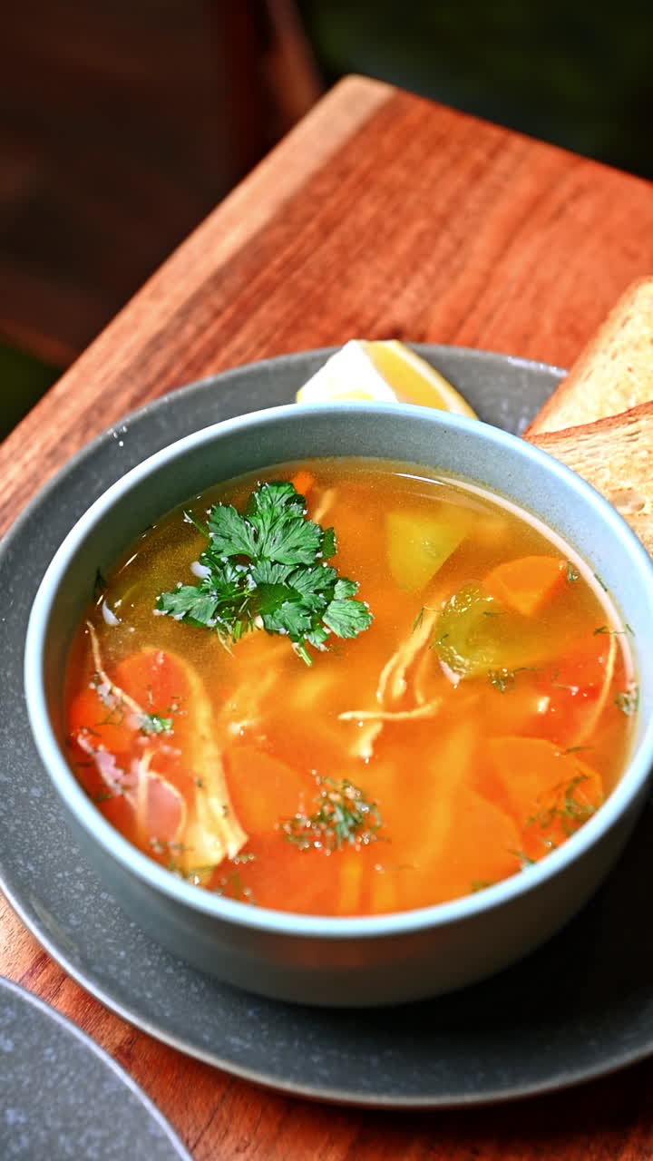 Bowl of hot chicken soup with vegetables and herbs. Homemade clear chicken broth with vegetables and parsley served in gray ceramic bowl
