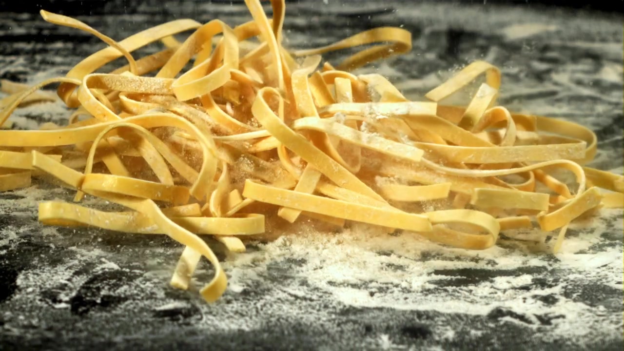 Pasta fresca fatta in casa che cade su una superficie scura infarinata