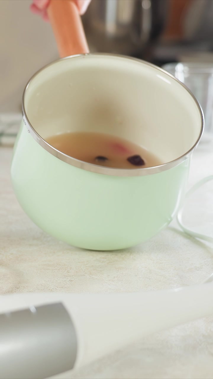 Hand interacts with various kitchen items including green mug. Hand grasps handles turns knobs and tilts saucepans revealing. Kitchen appliances glasses and checkered cloth are