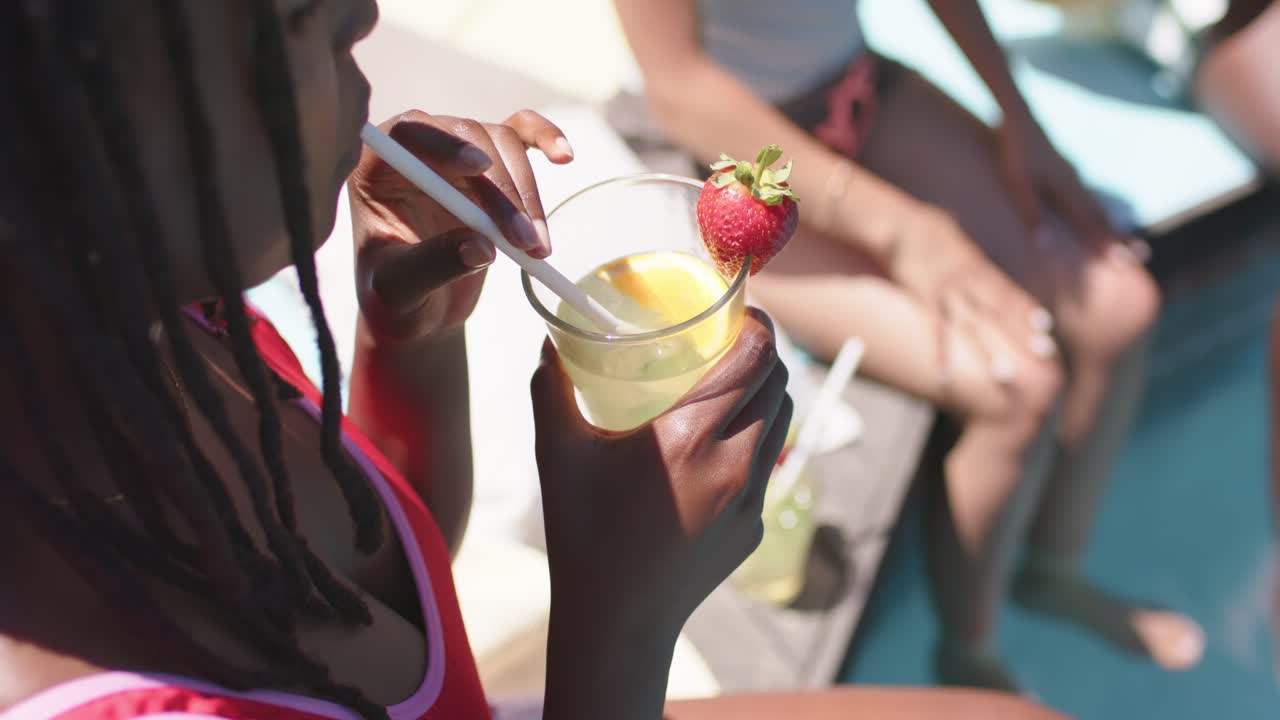 Hand is reaching and stirring clear cup with white straw and strawberry at poolside for sipping