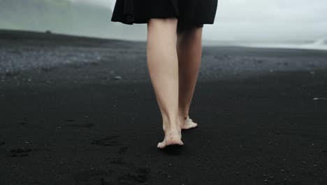 Pies-Caminando-En-La-Playa-De-Arena-Negra,-Islandia,-Hermosa-Mujer-Vestida-De-Negro,-Seguimiento-En-Cámara-Lenta,-Espectacular-Paisaje-Marino