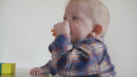 small-baby-nibbles-orange-toy-standing-at-table-in-room