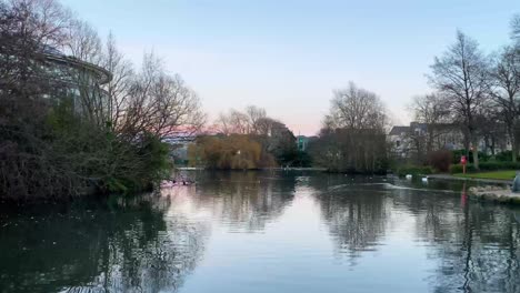 Schwenkaufnahme-Eines-Stadtparks-Mit-See-Bei-Sonnenuntergang