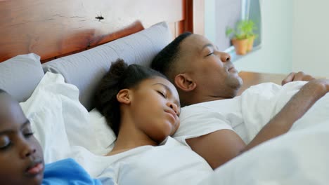 Front-view-of-young-black-family-sleeping-together-on-bed-in-bedroom-of-comfortable-home-4k