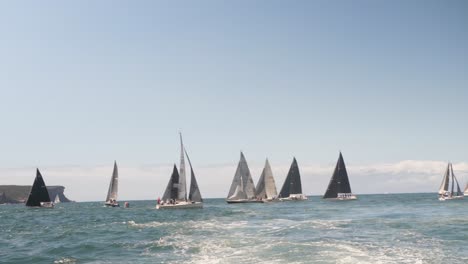 view from the back of a boat of many sail boats on the ocean practicing a race