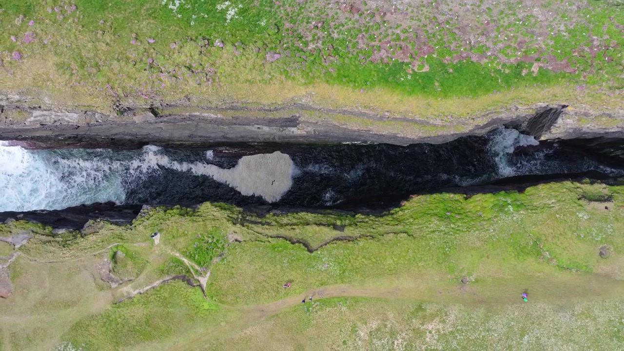 Wellen schlagen gegen die felsigen Klippen von Loop Head, Irland. Die Luftaufnahme fängt die dramatische Küstenlinie und üppiges Grün ein. Ideal für Reiseinhalte oder geografische Dokumentationen