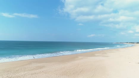 Aerial-panning-view-from-sand-beach-to-blue-sea-water-over-person-walking-a-dog