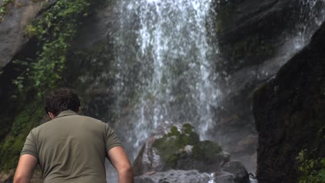 feliz divertido hombre de viaje emocionado y disfruta de una cascada tropical. sonriente turista masculino con máscara de cara tonto alrededor y diversión en el parque natural.