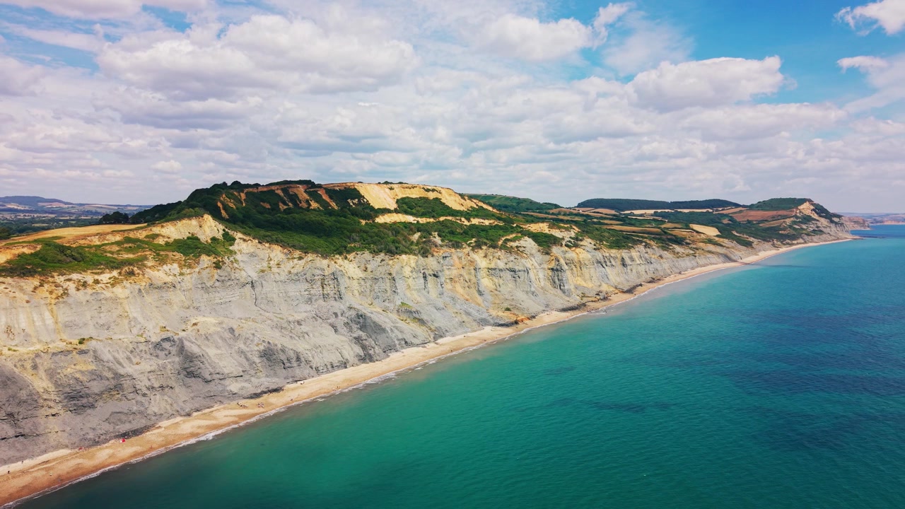 Rozległy materiał filmowy z drona ukazujący dramatyczne, erodowane klify, wąską plażę i turkusowe morze w pobliżu Charmouth na Wybrzeżu Jurajskim Dorset w Anglii. Widok wybrzeża podkreśla osuwisko