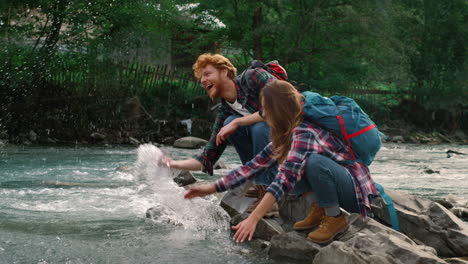 Woman-and-man-sitting-on-bank-of-river.-Hikers-splashing-water-from-stream