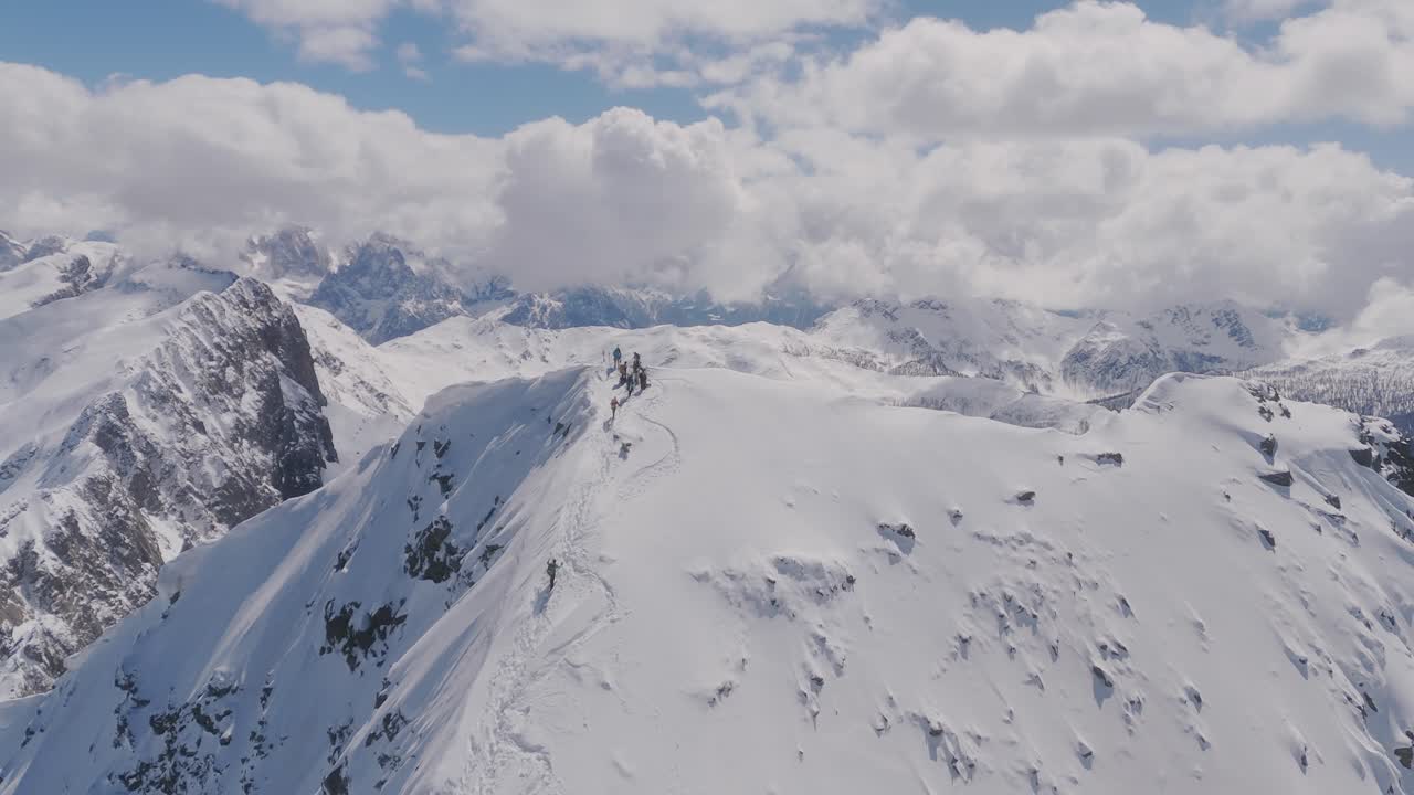 Escursionisti che attraversano una cresta montuosa innevata in un vasto paesaggio alpino.