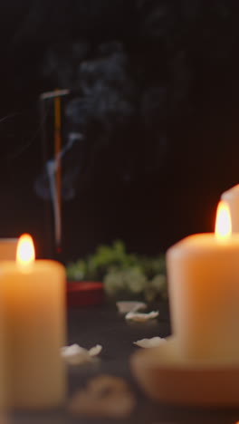 vídeo vertical ainda vida de velas acesas com pétalas espalhadas incenso stick contra fundo escuro como parte da decoração de dia de spa relaxante