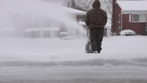 man clearing driveway with a snowblower on a snowy day