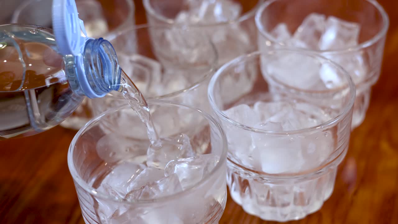 Acqua minerale limpida si versa da una bottiglia di plastica in un bicchiere pieno di cubetti di ghiaccio