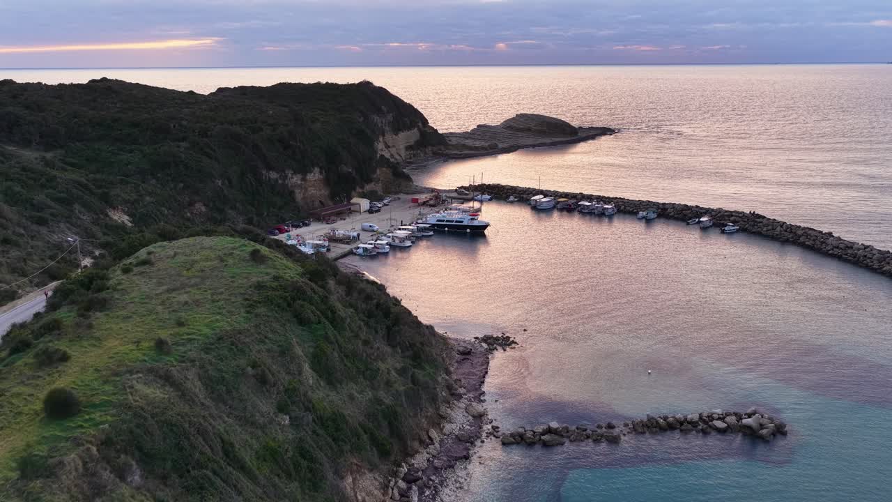 Vista aerea cinematografica di yacht di lusso e pescherecci ormeggiati al porto di Agios Stefanos, Corfù, Grecia, durante un bellissimo crepuscolo serale con riflesso sull'acqua