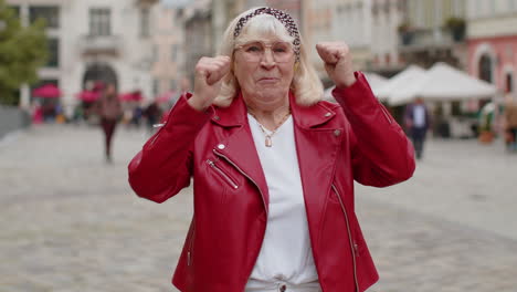 Senior-woman-shouting,-celebrating-success-winning-goal-achievement-good-victory-news-in-city-street