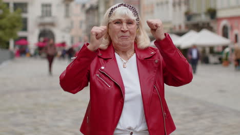 senior woman shouting, celebrating success winning goal achievement good victory news in city street