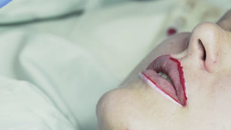 beautician makes permanent makeup on her lips. hands in blue rubber gloves hold a tattoo machine with red pigment. close up