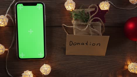 christmas donation concept: hand writing gift card and green screen smartphone