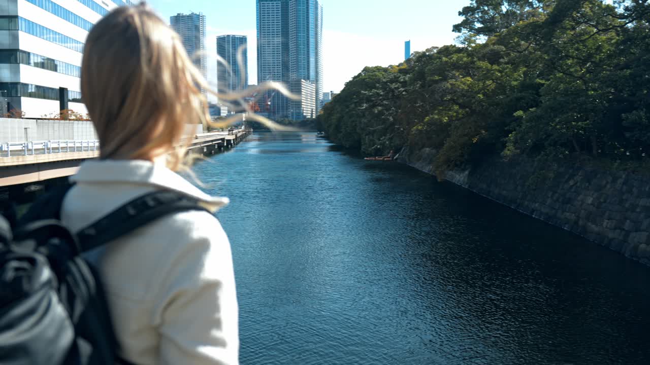 A peaceful scene of a woman walking through the beautiful Hamarikyu Gardens in Tokyo, surrounded by a tranquil mix of traditional Japanese landscapes and modern city skyscrapers.