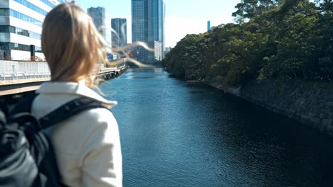 a peaceful scene of a woman walking through the beautiful hamarikyu gardens in tokyo, surrounded by a tranquil mix of traditional japanese landscapes and modern city skyscrapers.