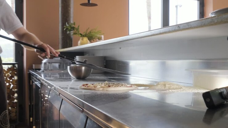 Chef che tiene una pizza su un vassoio nella cucina di un ristorante.