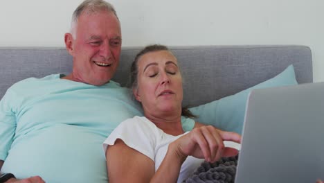 caucasian senior couple using laptop in bed at home