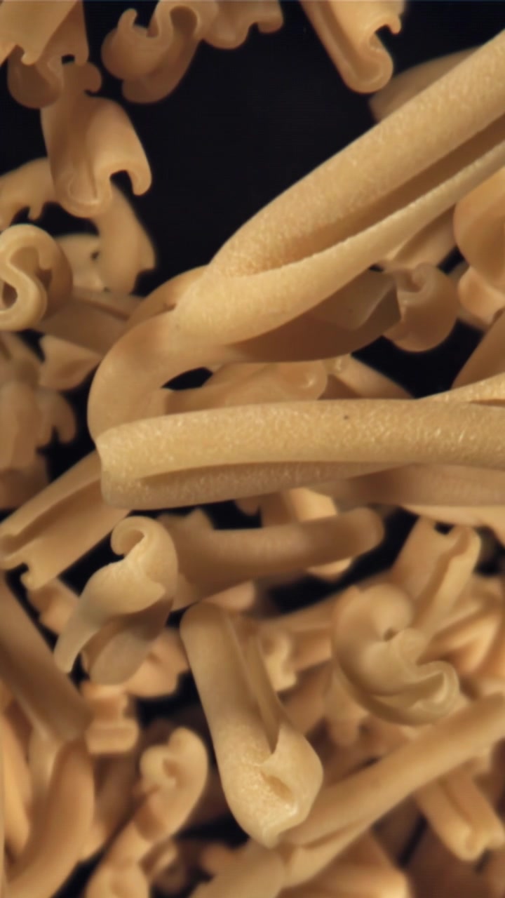 Ripresa verticale di pasta secca che cade al rallentatore su sfondo nero