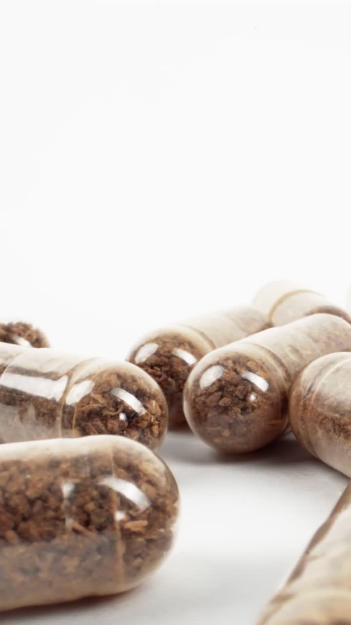 cápsulas transparentes con polvo de hierbas marrón sobre un fondo blanco