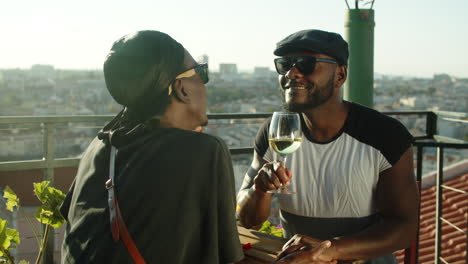 Happy-gay-couple-sitting-at-table-on-rooftop-and-kissing