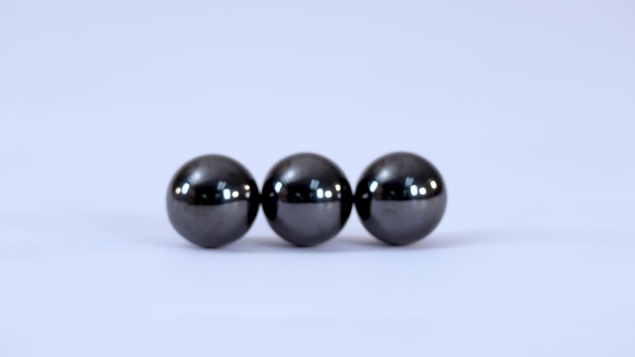 Three metallic magnetic balls roll together and connect on a plain white studio background