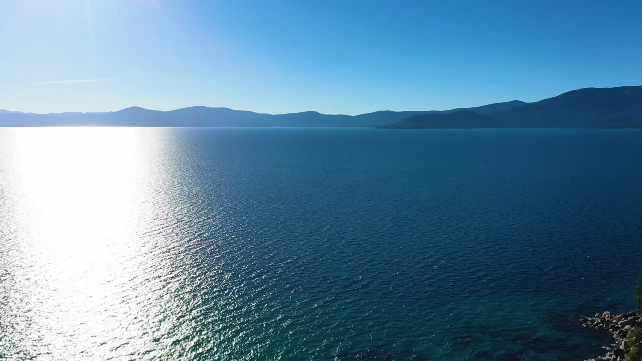 hermoso lago taho en california con montañas en el fondo y sol brillando en la superficie mientras el viento agita las olas a través de aguas cristalinas azules con embarcadero de roca en la costa