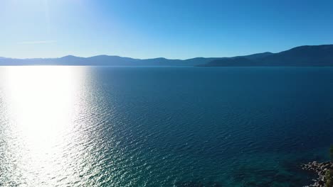 beautiful lake taho in california with mountains in the background and sunshine glistening off the surface as wind ripples waves across blue crystal clear water with rock jetty on shore