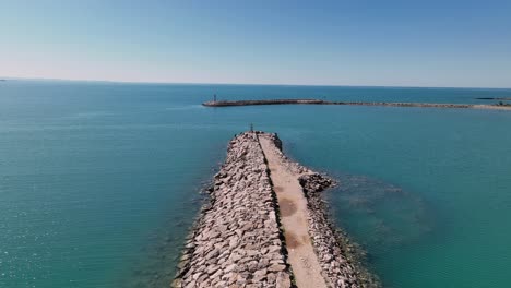 dolly aéreo a lo largo del rompeolas del embarcadero del puerto con pescadores en el punto