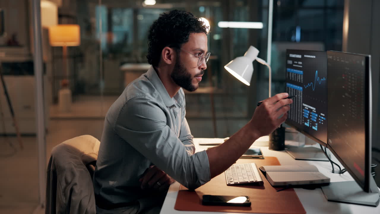 Man Working Late in Office Analyzing Data on Computer Screens